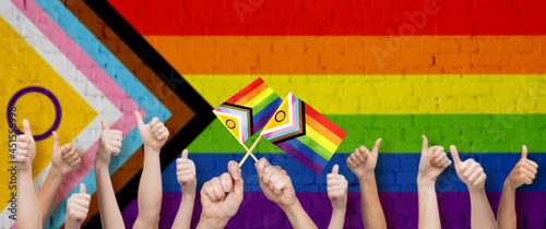 lgbtq, trans and intersex rights concept - multiracial human hands showing thumbs up over rainbow progress pride flag on background
