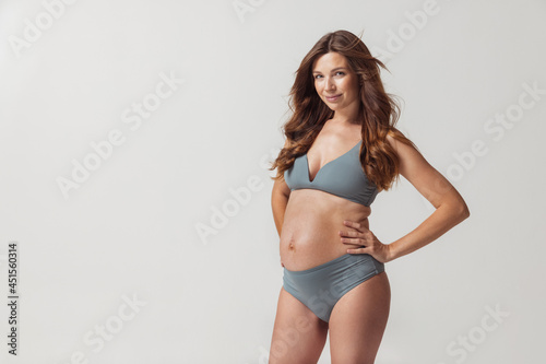 Portrait of beautiful pregnant woman in lingerie isolated over grey studio background. Natural beauty, happy motherhood, femininity concept. © master1305