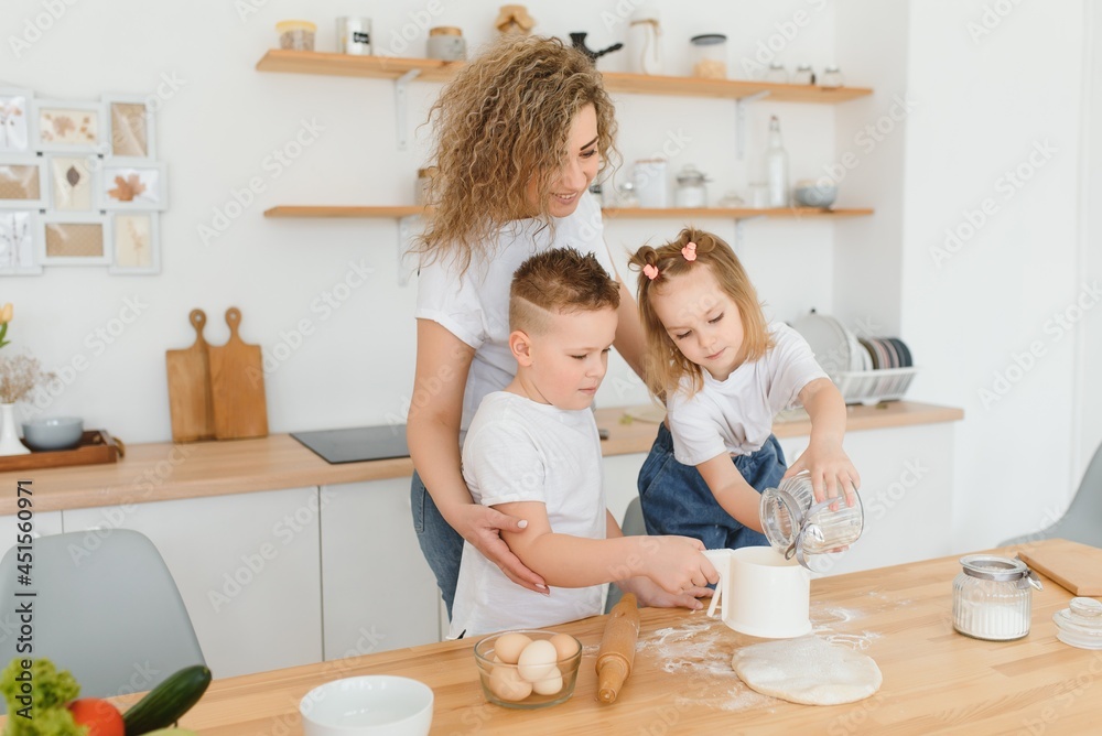 Happy young mother with cute little preschooler kids have fun making dough baking pie or pastry in modern kitchen together, overjoyed mother teach small children doing bakery cooking at home Happy young mother with cute little preschooler kids have fun making dough baking pie or pastry in modern kitchen together, overjoyed mother teach small children doing bakery cooking at home