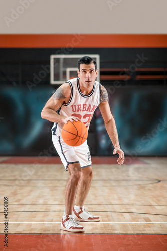 Dark-haired athletic man playing basket-ball in the gym