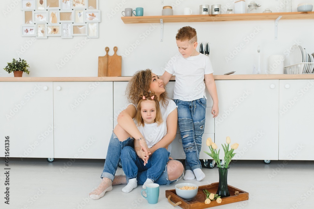 Happy young family, mom with little children sit on warm wooden floor in new modern design kitchen, mother with excited small kids relax rest in own renovated apartment, moving concept Happy young family, mom with little children sit on warm wooden floor in new modern design kitchen, mother with excited small kids relax rest in own renovated apartment, moving concept