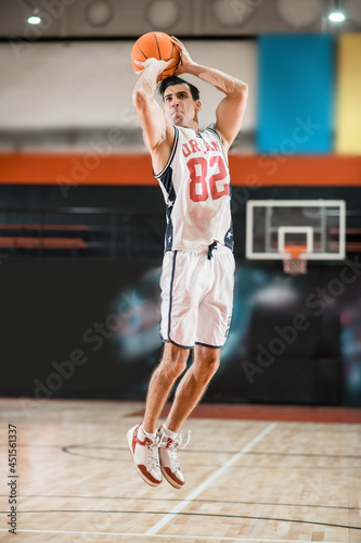 Young athletic man in white sportwear jumping with a ball in hands