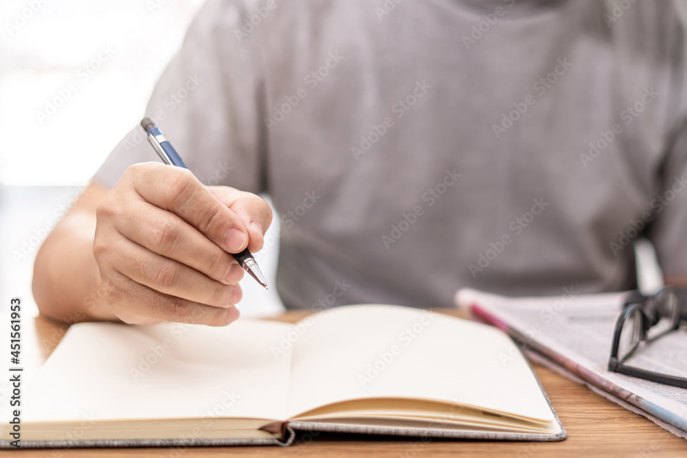 Close up hand a man hold pencil for write on the note book and newspaper glasses on wood table Close up hand a man hold pencil for write on the note book and newspaper glasses on wood table