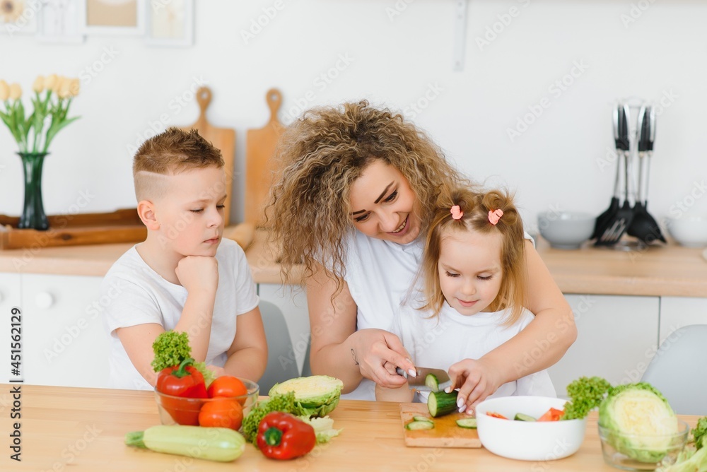 mother with children preparing vegetable salad at home