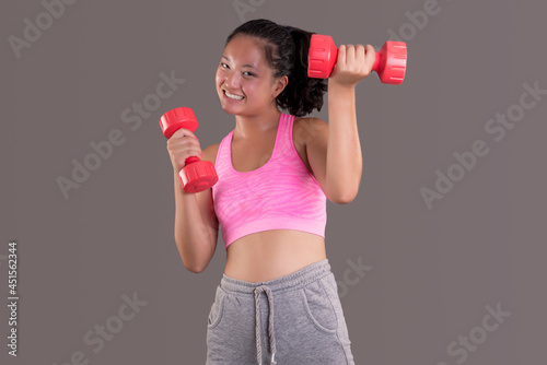 young chinese sports girl smiling while looking straight ahead and holding a dumbbell in her hands.
