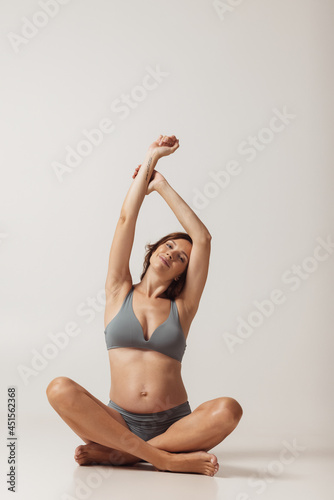 Portrait of pregnant sportive woman in lingerie isolated over grey studio background. Natural beauty, happy motherhood, femininity concept. © master1305