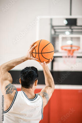 Dark-haired basket-ball player throwitn a ball into the ring