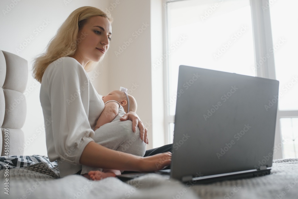 young woman with a small child works from home. Working remotely during a lockdown. freelancer or remotely employed specialist is sitting on a bed with a laptop and trying to concentrate young woman with a small child works from home. Working remotely during a lockdown. freelancer or remotely employed specialist is sitting on a bed with a laptop and trying to concentrate