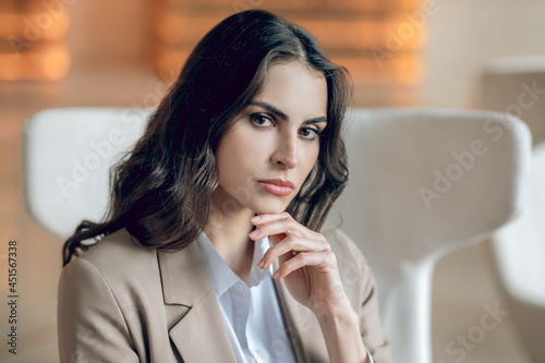 Pretty businesswoman sitting in the armchair and looking thoughtful