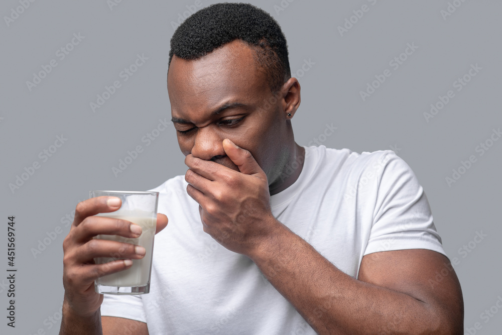 A dark-skinned man in a white thsirt holding a glass with milk A dark-skinned man in a white thsirt holding a glass with milk