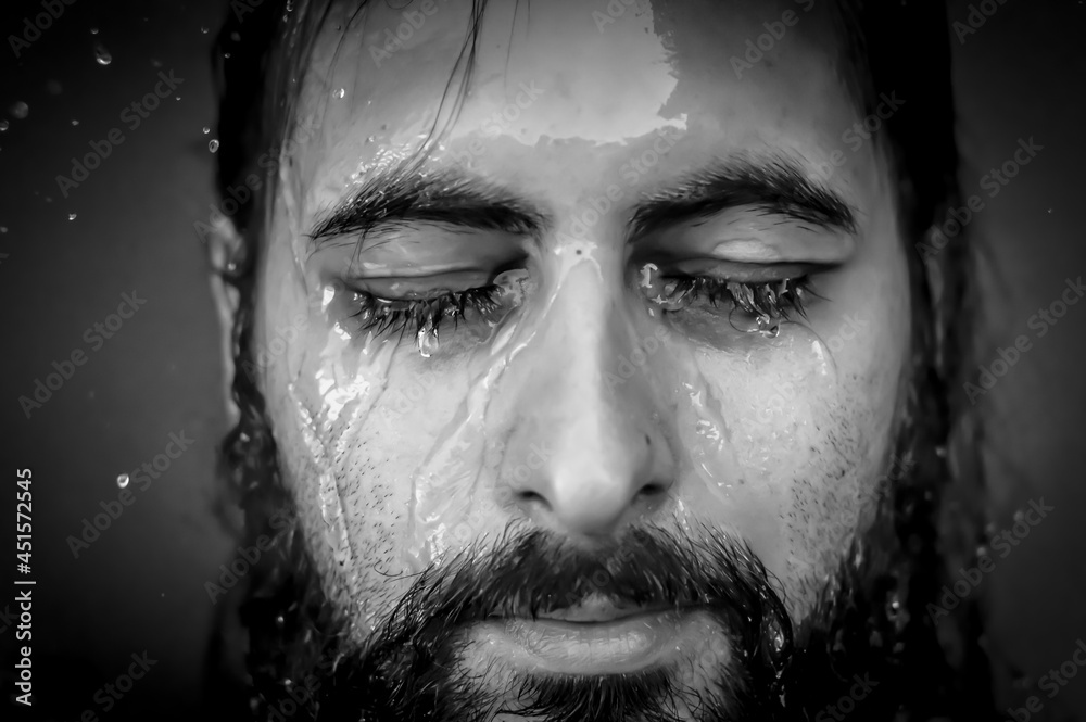 Black and white very close-up portrait of a young bearded man with closed eyes with streams of water running down his face