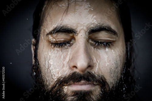 Very close-up portrait of a young bearded man with closed eyes and streams of water running down his face 