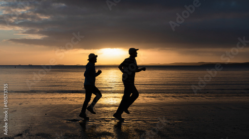 Silhouette of two people running on sand beach at sunrise