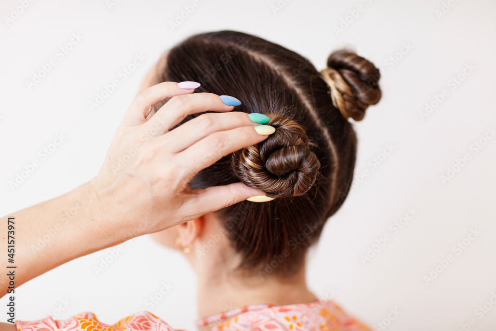 Naklejka premium A young woman fixes her hair bun. She wears rainbow gradient manicure.