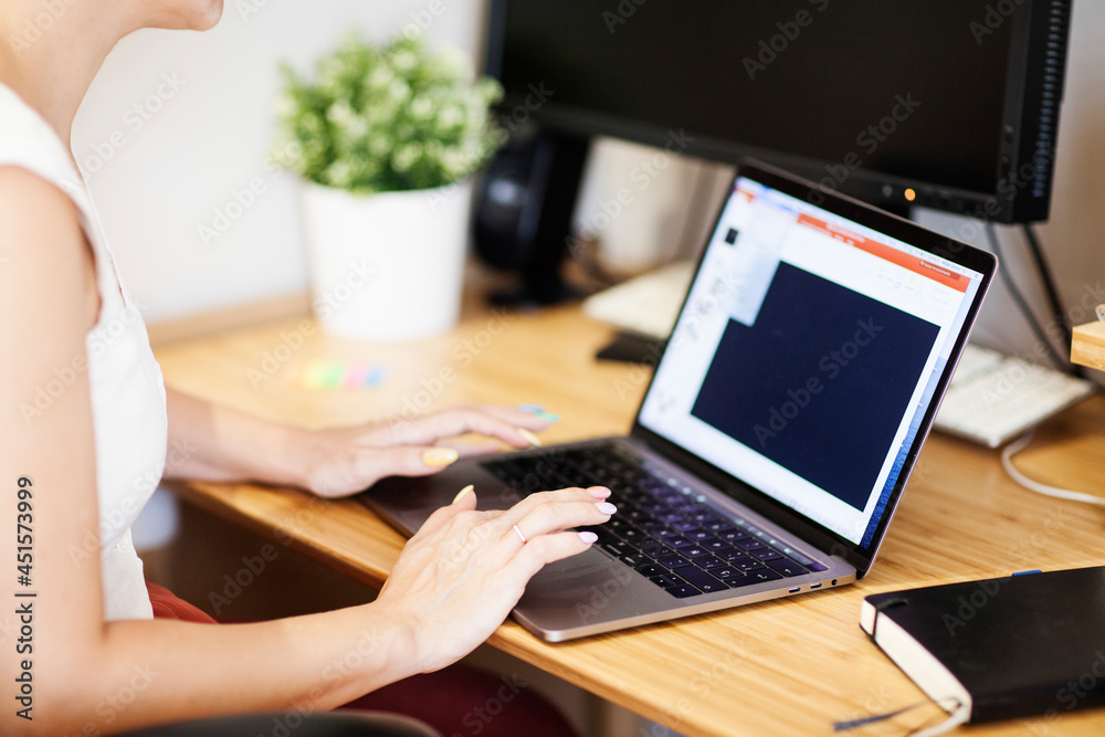 Naklejka premium A young woman types on her laptop on a wooden desk as she works.