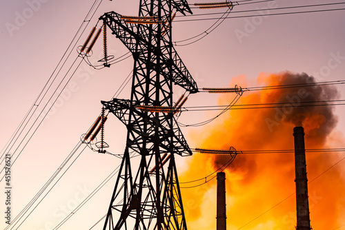 High voltage electric lines and industry. Pipes with dark smoke near the transmission electric towers at dusk. Pollution the atmosphere concept