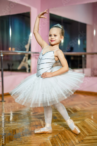 A little girl in a white tutu standing in pose with hand over head near the mirror. Children and ballet concept