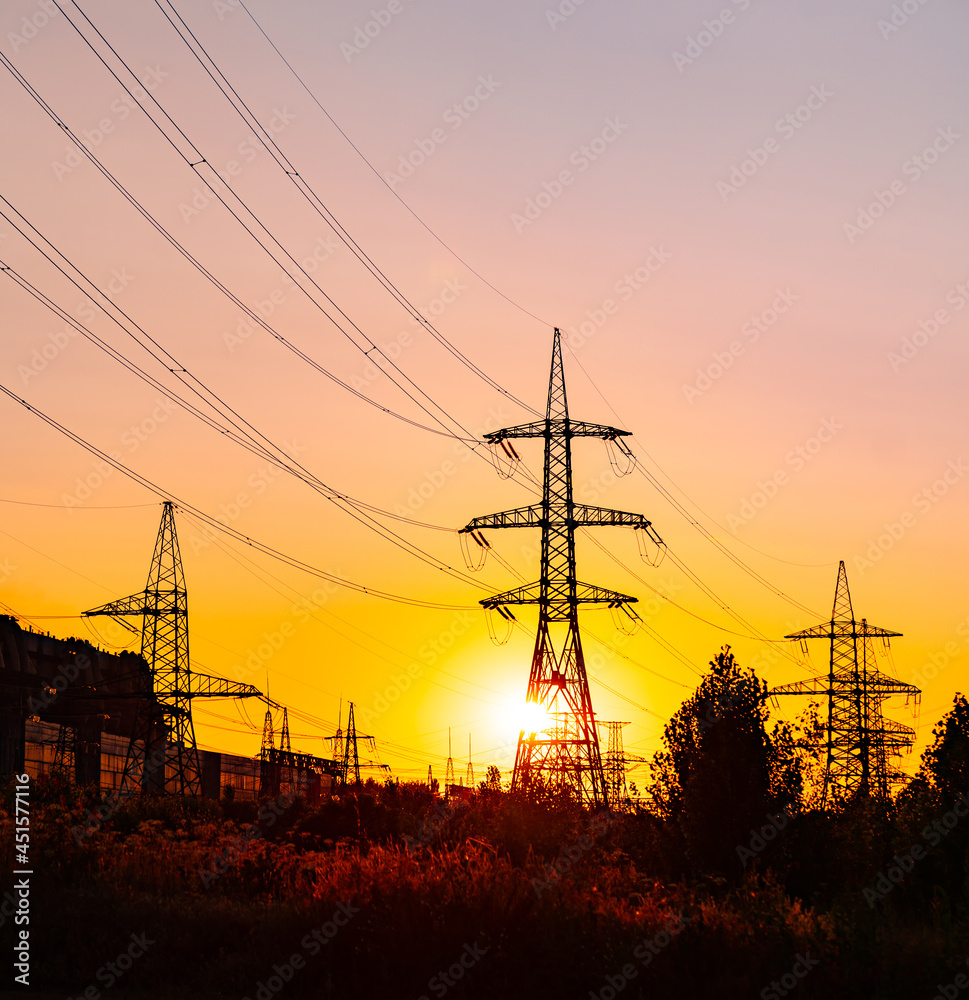 Transmission lines against the evening sky. High-voltage electric towers with wires on the setting sun background. Black pylons with electricity