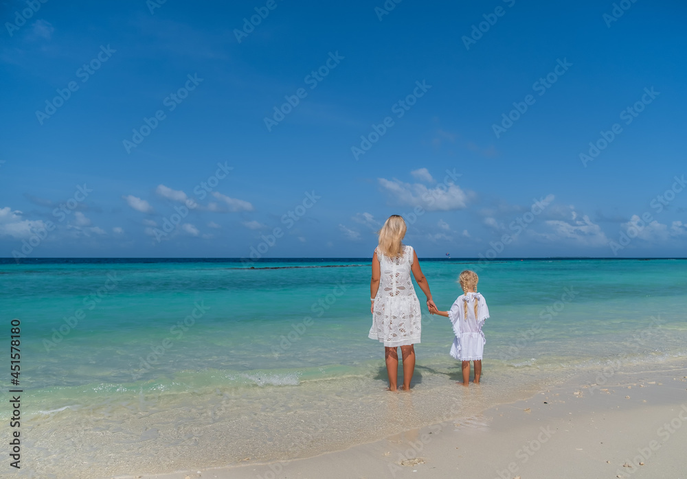 Beautiful mother and little daughter watching on the ocean from the tropical Maldivian beach. Crossroads Maldives, july 2021