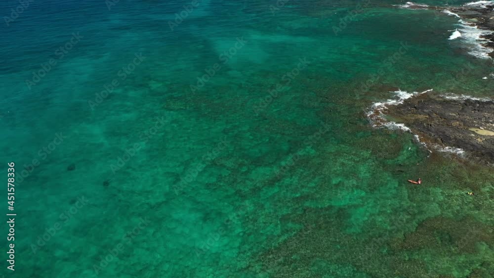 Bird's eye aerial drone view of Hawaiian coral reef on the island of Oahu in Hawaii, USA. Clear, turquoise-green water with visible reef below. Bird's eye aerial drone view of Hawaiian coral reef on the island of Oahu in Hawaii, USA. Clear, turquoise-green water with visible reef below.