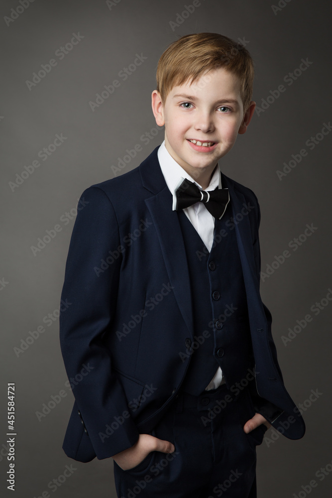Elegant Little Boy in Classic Black Suit with Bowtie over Gray. Smiling Child Gentleman in Smart Casual Clothing. School Kids Fashion Elegant Little Boy in Classic Black Suit with Bowtie over Gray. Smiling Child Gentleman in Smart Casual Clothing. School Kids Fashion