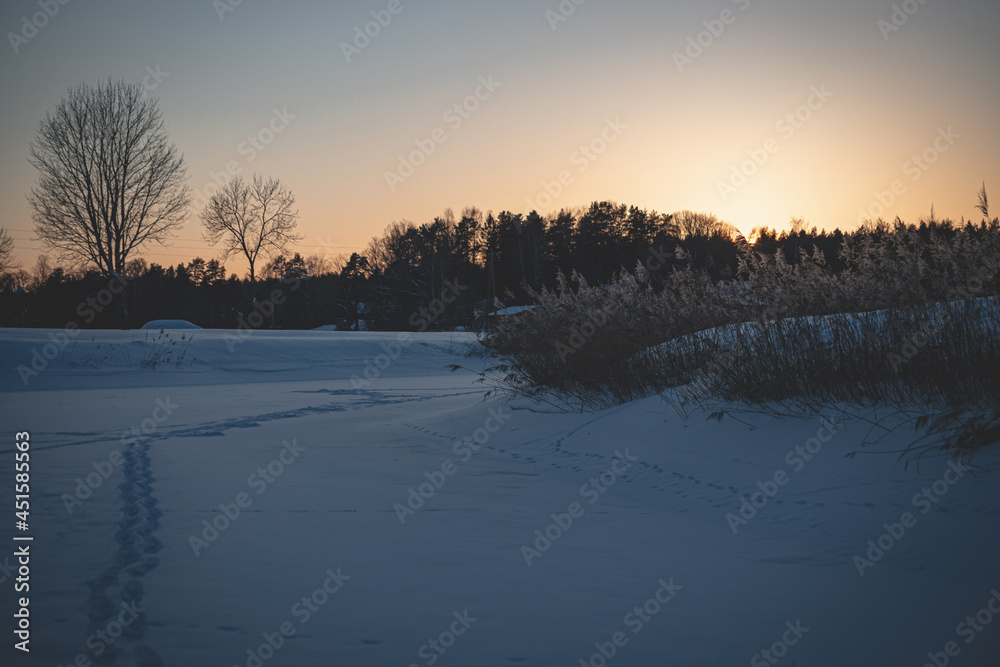 footpath down a snow-covered slope on the river bank, Footprints in the snow of a frozen river in winter evening sunset footpath down a snow-covered slope on the river bank, Footprints in the snow of a frozen river in winter evening sunset