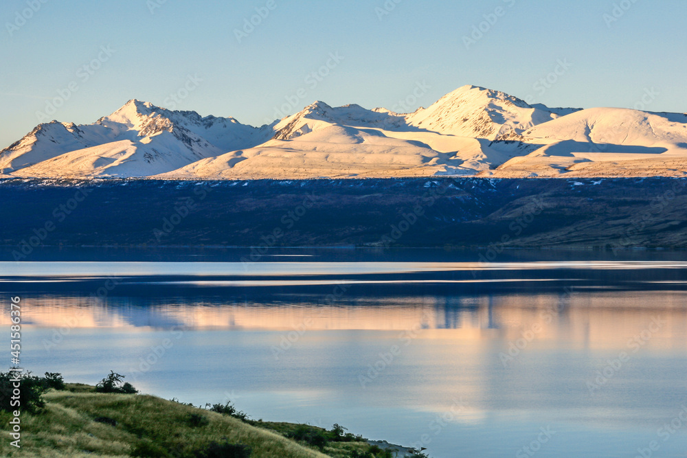 A mountain range reflected on a calm lake on a clear, blue day with light and shadow