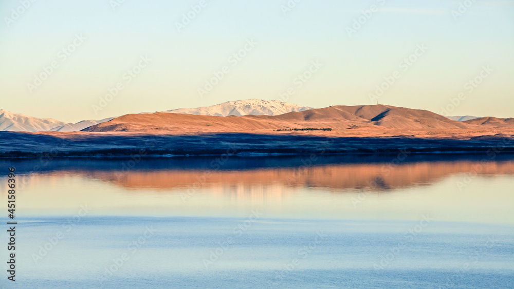 A mountain range reflected on a calm, blue lake on a fresh, clear day