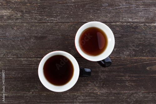 A pair of cups with black tea on the background of a table made of wooden boards.