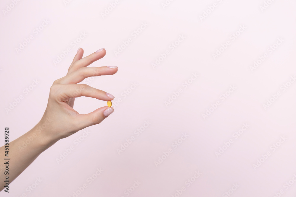 Woman hand holding yellow pill capsule on a pink background, medication concept with copy space Woman hand holding yellow pill capsule on a pink background, medication concept with copy space