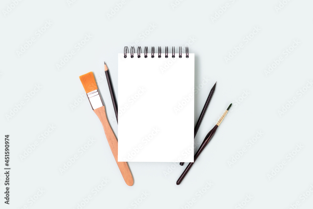 Empty notepad mockup and tools for painting on a blue pastel background. Notebook, paintbrush and pencil with copyspace. Artistic workspace. Empty notepad mockup and tools for painting on a blue pastel background. Notebook, paintbrush and pencil with copyspace. Artistic workspace.