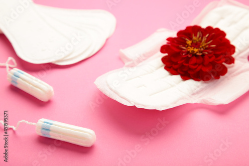 Menstrual tampons and pads on pink background. Menstruation cycle. Hygiene and protection. A rose flower lies on a menstrual pad.