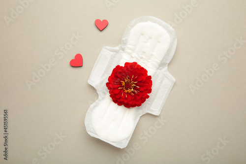 White sanitary pad, hygiene protection on a grey background. Gynecological menstrual cycle. A rose flower lies on a menstrual pad. First menstruation