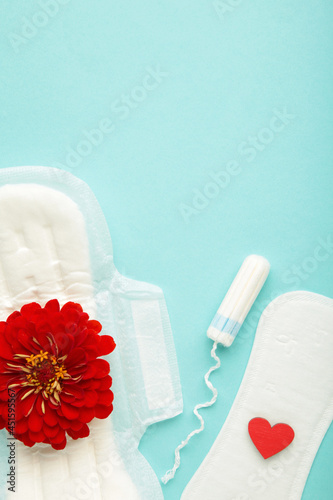 Menstrual tampons and pads on blue background. Menstruation cycle. Hygiene and protection. A rose flower lies on a menstrual pad. photo