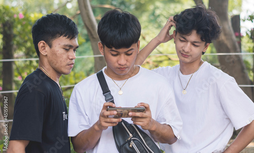 A young man plays online games on his cellphone while two of his friends watch on. One of them is unimpressed at his skill. photo