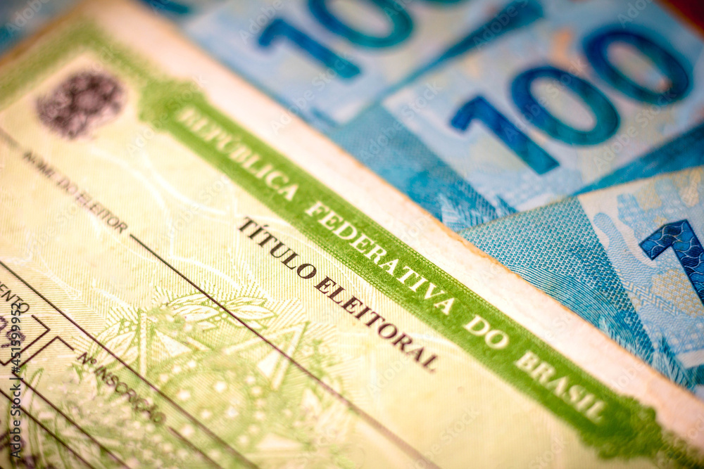 Obraz premium In this photo illustration the Voter License (Título Eleitoral). Photo election vote card (voter id). One hundred reais bills in the background.