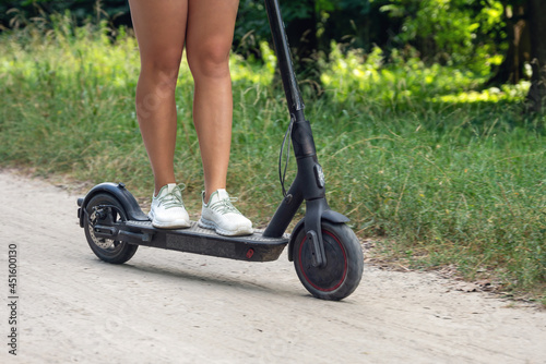 Female feet on an electric scooter riding on a dirt road
