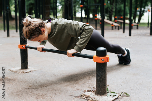 Sporty young fit woman in sportswear exercising on playground doing physical strength exercise, bar push-ups, fitness morning workout outdoors. Healthy active lifestyle concept