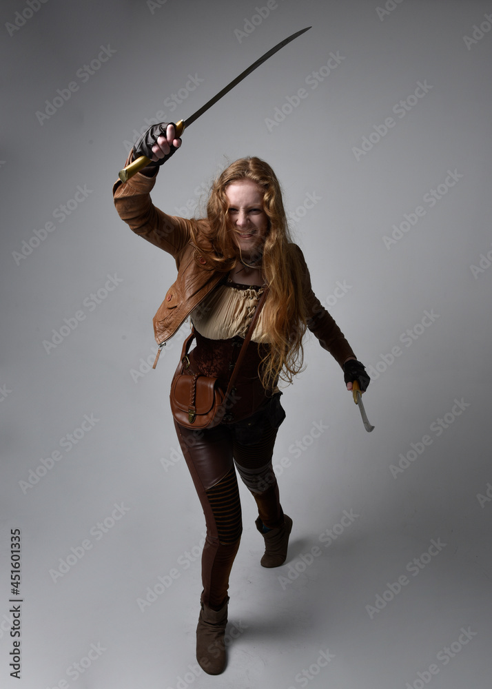 Full length portrait of beautiful young woman with long red hair, wearing steampunk inspired costume knife weapons isolated on studio background. Full length portrait of beautiful young woman with long red hair, wearing steampunk inspired costume knife weapons isolated on studio background.