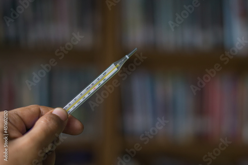 Hand holding mercury thermometer glass tube with a blurry background. Horizontal, copy space for text. 