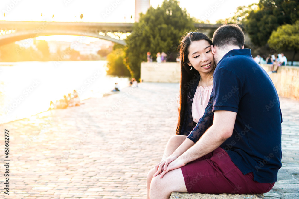 Multiracial couple sitting by the river with a sunset.