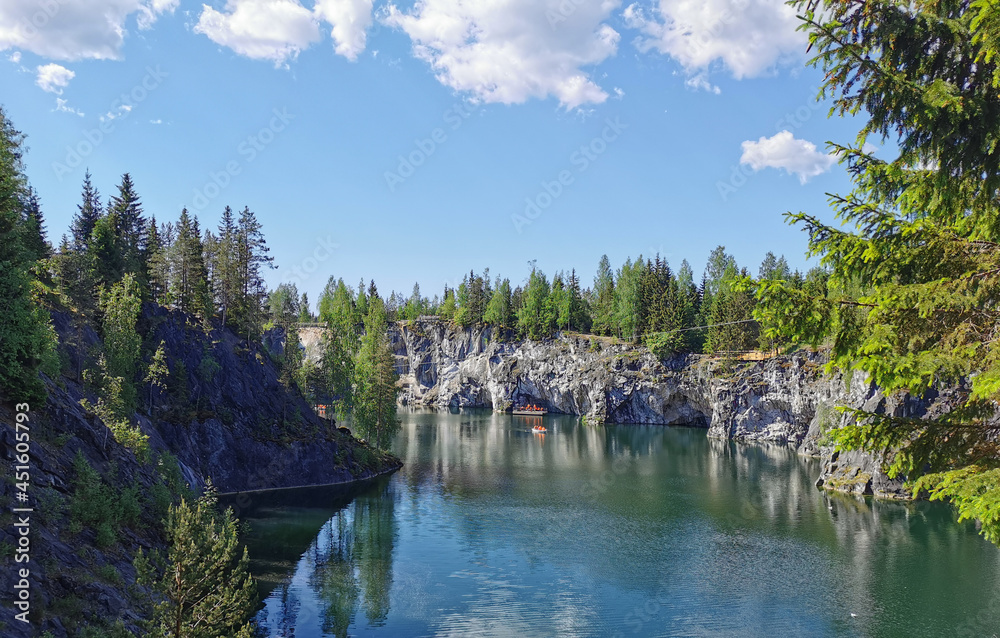View from the observation deck of the emerald water of the Marble Canyon in the Ruskeala Mountain Park with the reflection of the sky and clouds on a sunny summer day.