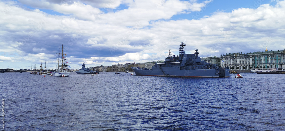 Panoramic view of warships and sailboats in the Neva water area for the Day of the Navy in St. Petersburg against the background of the Winter Palace.