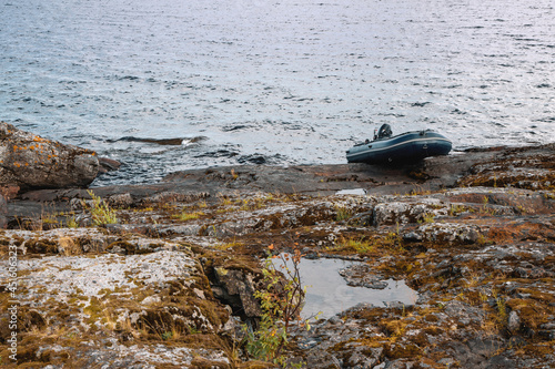 An inflatable rubber boat with a motor stands on the stone shore