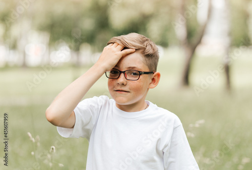 A cute freckled boy with glasses holds on to his head.