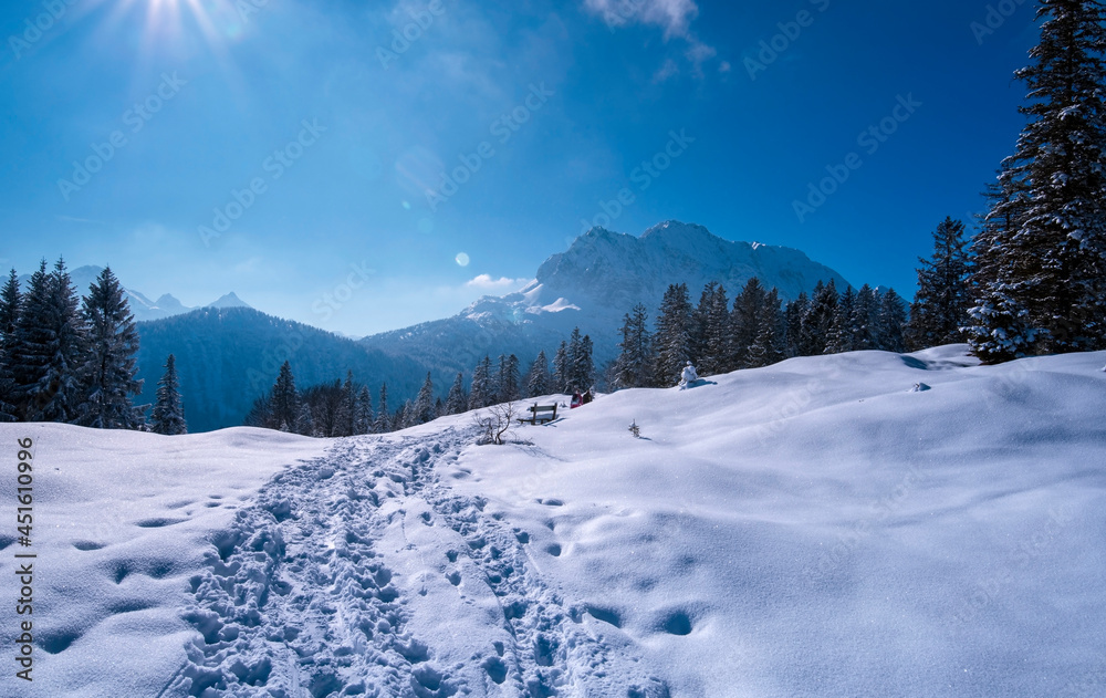 Schneelandschaft mit Bergpanorama in den bayerischen Alpen in einem Erholungsgebiet mit Wald und Wanderweg an einem sonnigen Tag