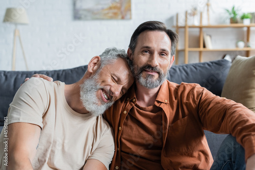 Mature man hugging smiling homosexual partner at home photo
