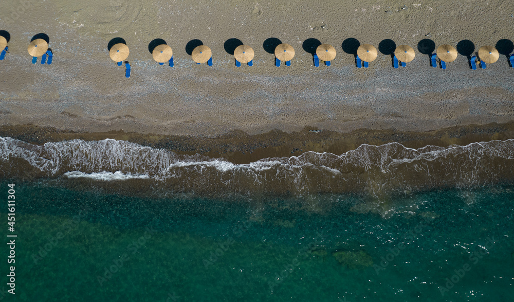 Aerial view from a flying drone of beach umbrellas in a row on an empty beach with braking waves.
