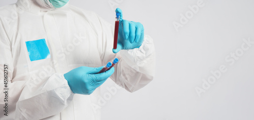Hand with PPE suit and blue medical glove is holding blood test tube on white background.