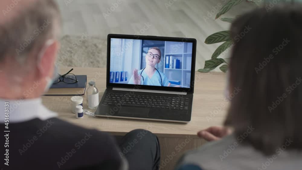 elderly couple in medical masks communicate with doctor online using modern video communication on laptop while sitting at home during quarantine elderly couple in medical masks communicate with doctor online using modern video communication on laptop while sitting at home during quarantine
